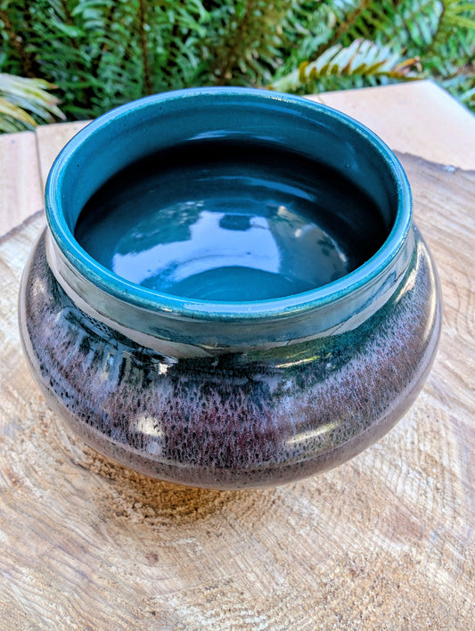 Ceramic bowl with blue interior and brown exterior on a wooden surface with greenery in the background