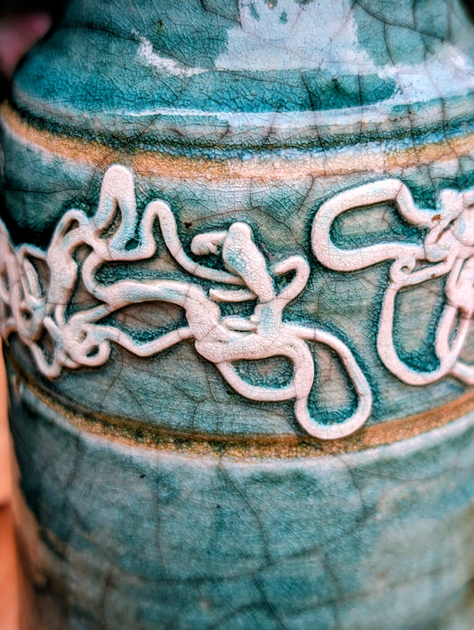 Celebrate the artistry of 1970s studio ceramics with this signed and dated handmade stoneware vase. Finished in a rich teal crackle glaze with distinctive white applied slip decoration, this sculptural piece brings timeless character to shelves, tables, and curated collections.