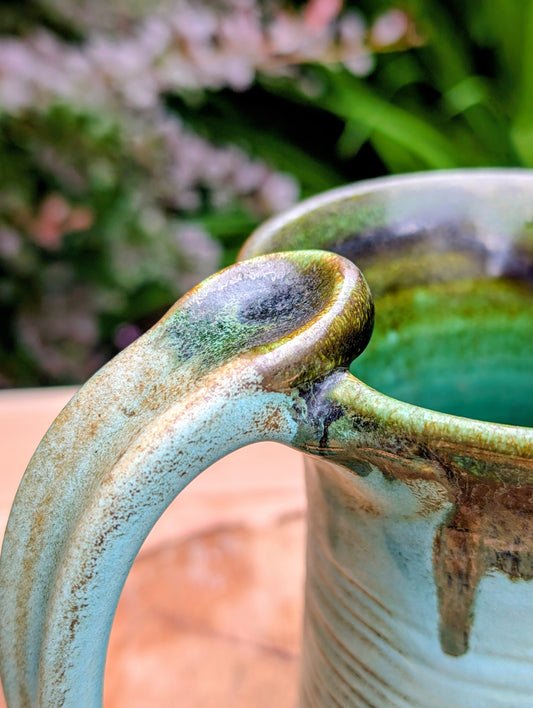 A beautifully handcrafted studio pottery tankard-style mug, wheel-thrown in Hot Springs, Arkansas and dated 2007. Its flowing turquoise, olive, and bronze glaze, generous size, and comfortable thumb-rest handle make it both a functional everyday piece and a collectible example of American studio pottery.