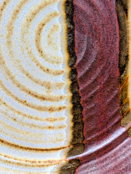 A striking hand-thrown studio pottery platter featuring an expressive cream, maroon, and olive glaze composition with visible throwing rings and an incised artist signature. Beautiful as both a decorative wall display and a functional serving piece, it embodies the warmth and craftsmanship of contemporary American studio ceramics.