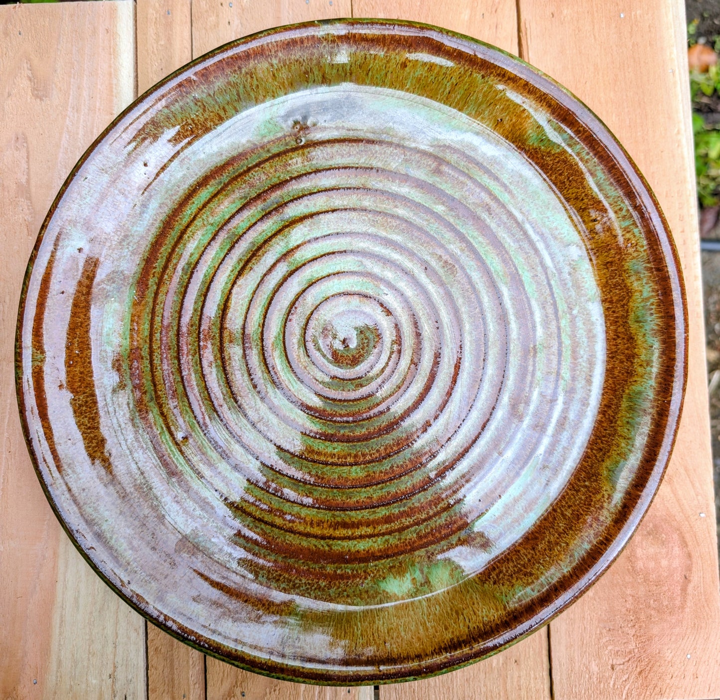 A beautifully hand-thrown studio pottery charger featuring an impressed spiral design and richly variegated moss green and rust glazes. This substantial signed stoneware piece brings timeless craftsmanship and Pacific Northwest-inspired warmth to shelves, tables, or wall displays.