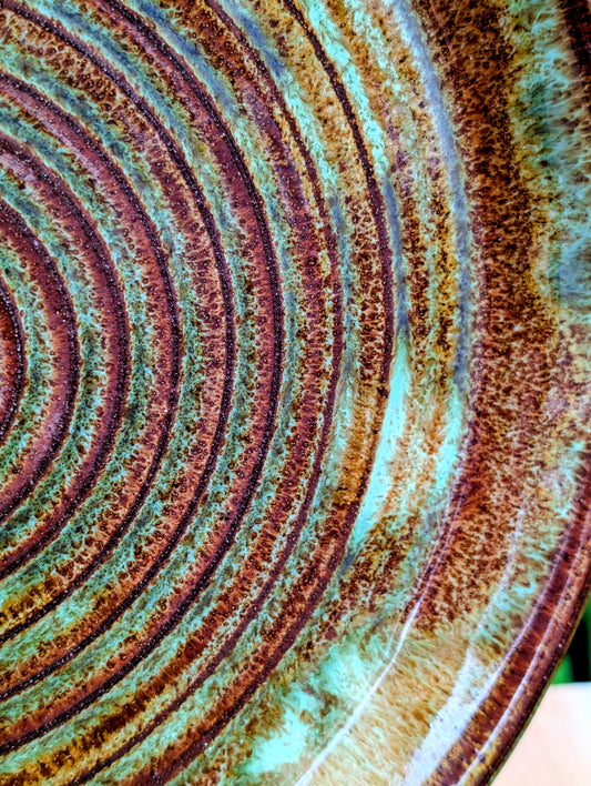 A beautifully hand-thrown studio pottery charger featuring an impressed spiral design and richly variegated moss green and rust glazes. This substantial signed stoneware piece brings timeless craftsmanship and Pacific Northwest-inspired warmth to shelves, tables, or wall displays.