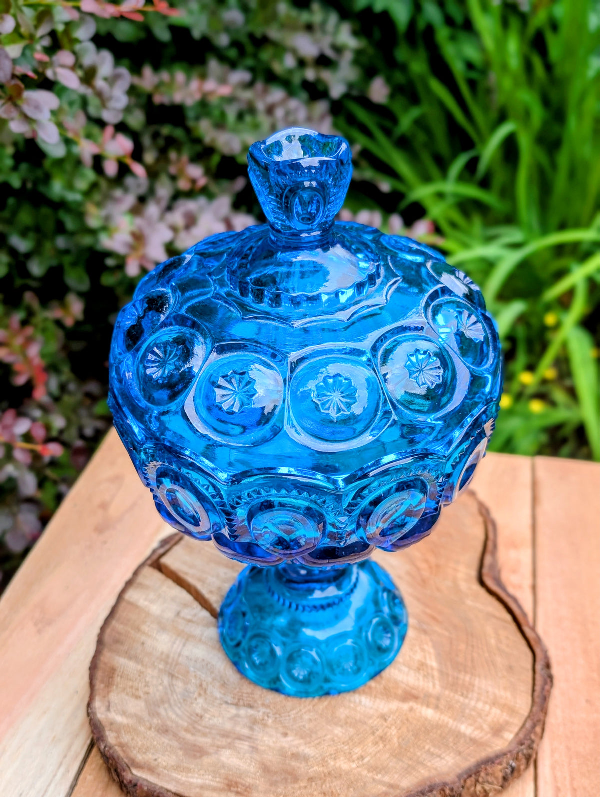 Bring timeless American glass craftsmanship into your home with this authentic L.E. Smith Moon and Stars covered pedestal candy dish in sought-after Colonial Blue. Its richly embossed pattern and luminous pressed glass make it equally beautiful as a centerpiece, candy dish, or collectible display piece.