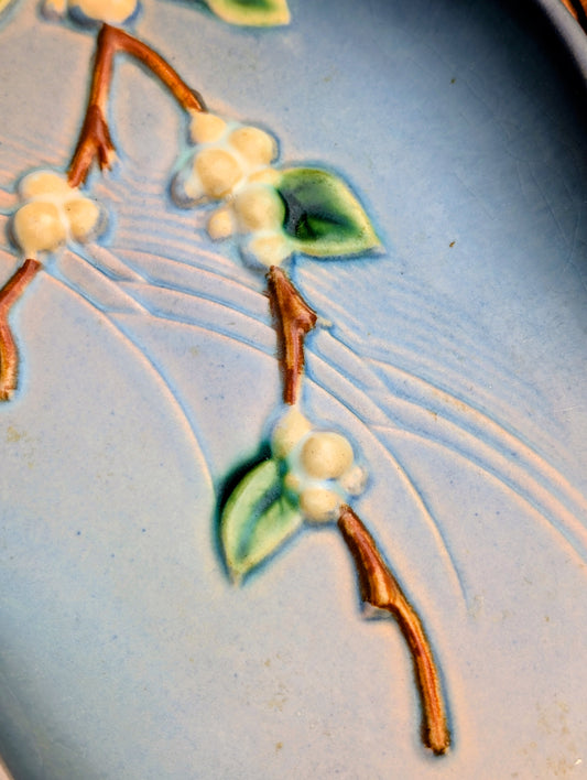 Close-up of a light blue ceramic surface with embossed floral details, including white blossoms, green leaves, and brown stems.