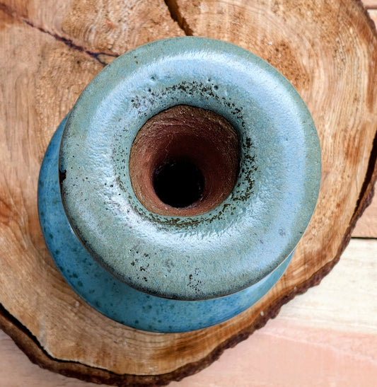 A beautifully hand-thrown studio pottery bud vase featuring a rich blue-green glaze over warm stoneware clay. Its timeless organic form makes it perfect for displaying a single bloom, dried botanicals, or as a sculptural accent in any room.