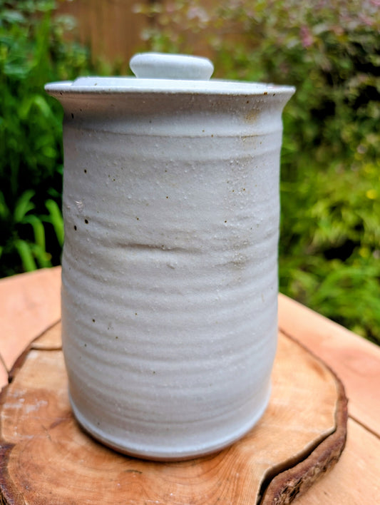 Bring warmth and handcrafted character to your kitchen with this wheel-thrown stoneware canister. Finished in a soft creamy-white glaze with subtle iron speckling, this timeless storage vessel blends rustic craftsmanship with modern organic design.