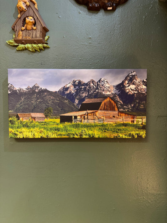 A striking mountain landscape featuring a weathered barn set against dramatic snow-capped peaks and an open meadow. This canvas artwork brings rustic character, natural beauty, and a sense of place to the home.