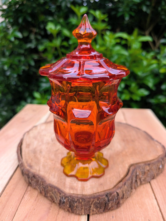 Bring a warm glow to your home with this vintage Fenton Valencia covered glass jar in vibrant Orange Amberina. Originally marketed as a cigarette box, this versatile Mid-Century piece now shines as a candy dish, apothecary jar, or decorative accent with timeless vintage appeal.