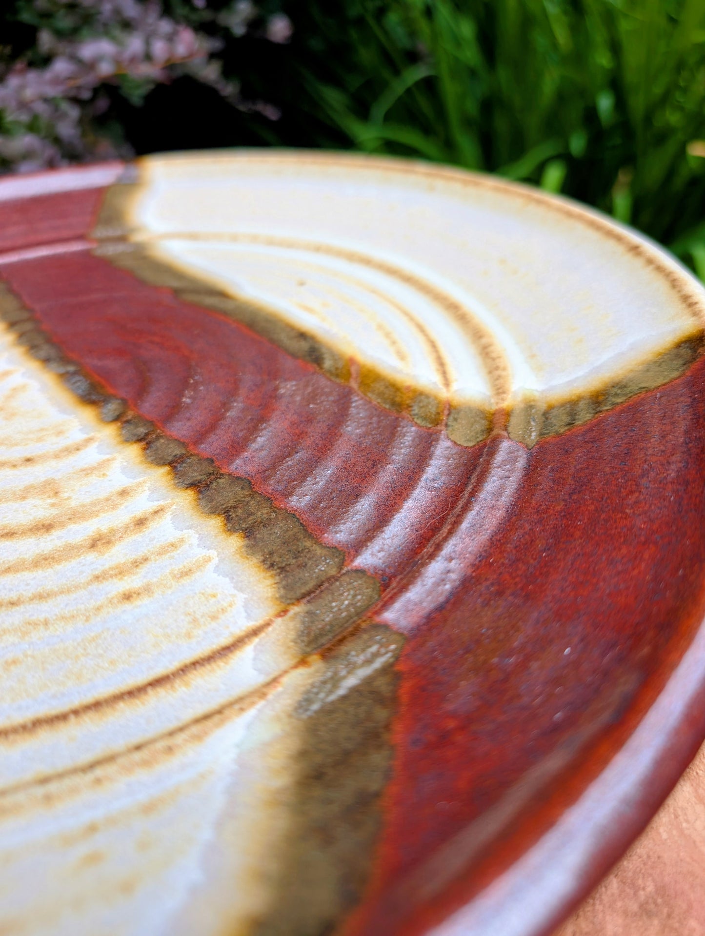 A striking hand-thrown studio pottery platter featuring an expressive cream, maroon, and olive glaze composition with visible throwing rings and an incised artist signature. Beautiful as both a decorative wall display and a functional serving piece, it embodies the warmth and craftsmanship of contemporary American studio ceramics.
