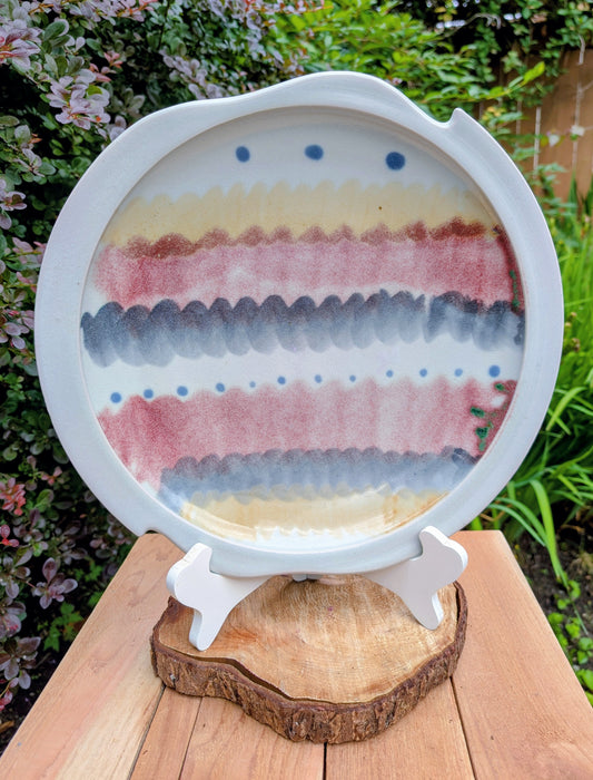A beautifully handcrafted 14-inch studio pottery platter featuring layered abstract decoration in soft blue-gray, dusty pink, cream, and cobalt accents. Equally stunning as a serving piece or decorative display charger, this artisan-made platter brings timeless craftsmanship to modern living.