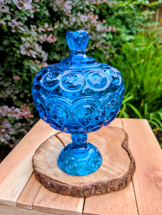 Bring timeless American glass craftsmanship into your home with this authentic L.E. Smith Moon and Stars covered pedestal candy dish in sought-after Colonial Blue. Its richly embossed pattern and luminous pressed glass make it equally beautiful as a centerpiece, candy dish, or collectible display piece.