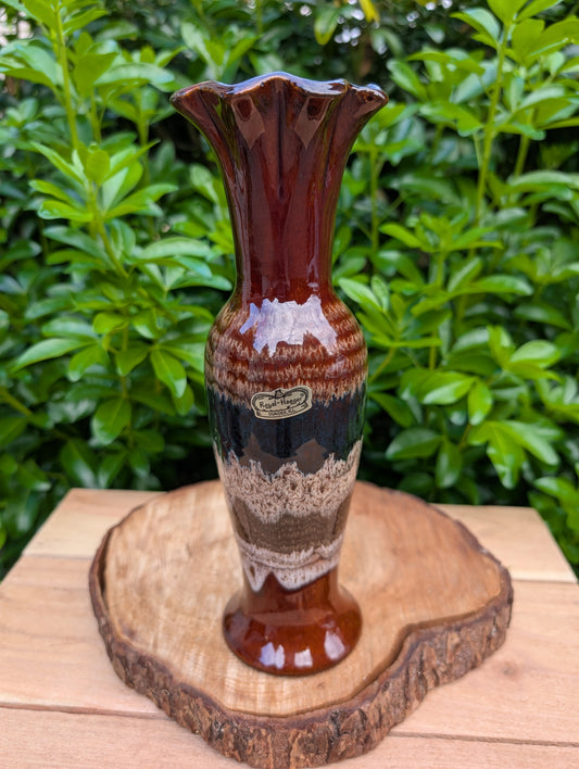 Bring warm earth tones and classic Mid-Century Modern style into your home with this vintage Royal Haeger trumpet vase. Featuring the iconic earth-wrapped lava drip glaze in rich browns, cream, and black, this elegant 10-inch vase is beautiful displayed with fresh florals, dried botanicals, or as a sculptural statement on its own.