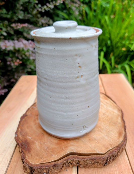 Bring warmth and handcrafted character to your kitchen with this wheel-thrown stoneware canister. Finished in a soft creamy-white glaze with subtle iron speckling, this timeless storage vessel blends rustic craftsmanship with modern organic design.