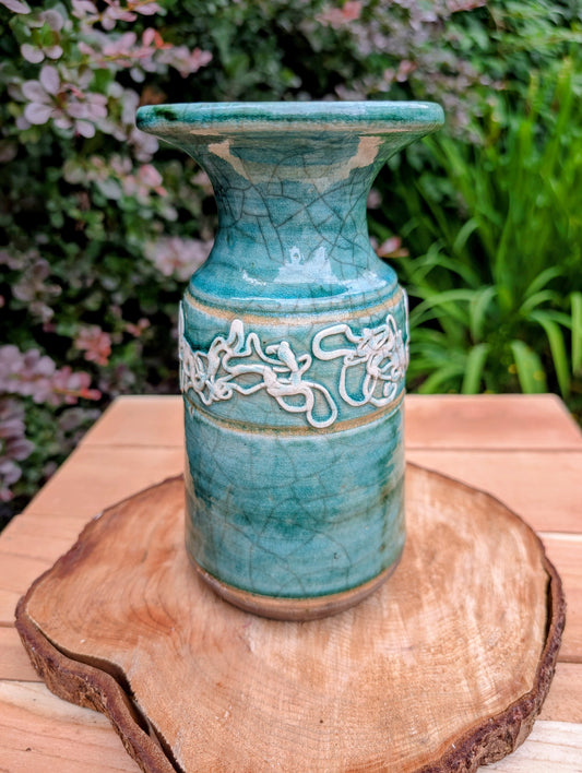 Celebrate the artistry of 1970s studio ceramics with this signed and dated handmade stoneware vase. Finished in a rich teal crackle glaze with distinctive white applied slip decoration, this sculptural piece brings timeless character to shelves, tables, and curated collections.