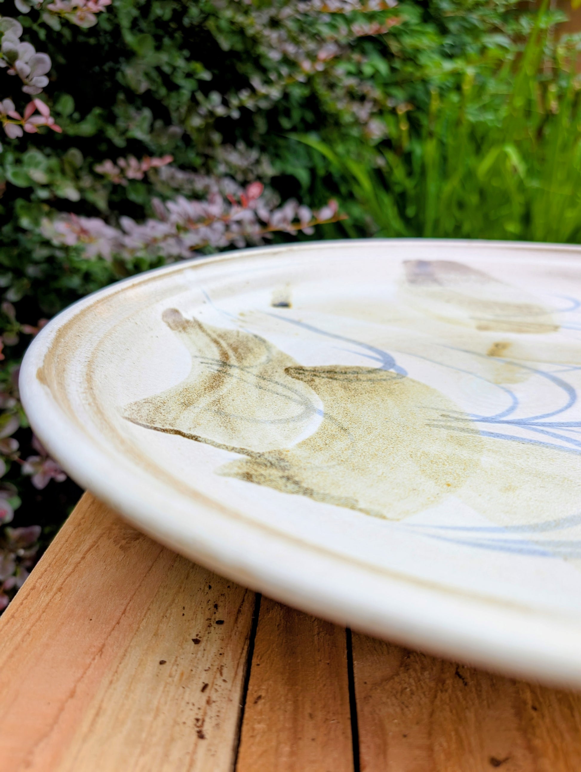 A beautifully hand-thrown studio pottery platter featuring expressive blue-gray and olive brushwork over a soft neutral glaze. Its generous size and timeless craftsmanship make it equally suited for serving, display, or as striking wall décor.