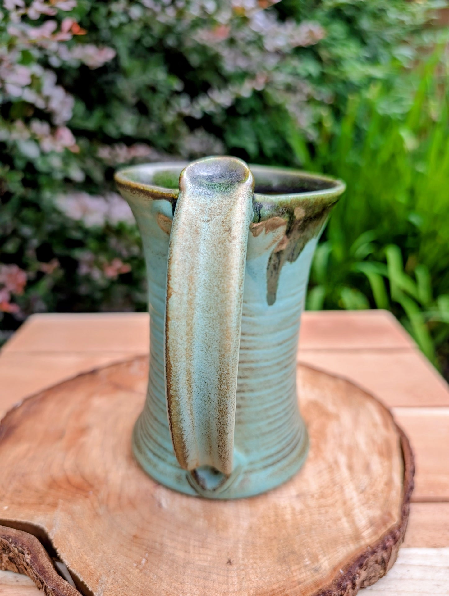 A beautifully handcrafted studio pottery tankard-style mug, wheel-thrown in Hot Springs, Arkansas and dated 2007. Its flowing turquoise, olive, and bronze glaze, generous size, and comfortable thumb-rest handle make it both a functional everyday piece and a collectible example of American studio pottery.