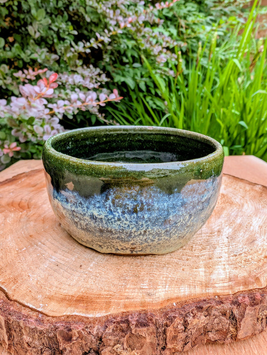A beautifully hand-thrown studio pottery bowl featuring a rich olive green interior and layered blue, cream, and earthy brown glaze. Signed by the artist, this compact stoneware piece blends functional craftsmanship with timeless Pacific Northwest style.
