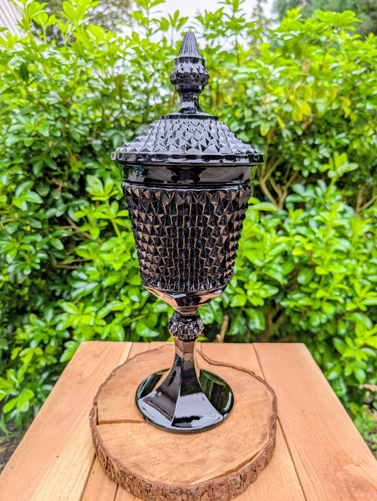 Make a dramatic statement with this vintage Tiara Exclusives Diamond Point covered pedestal compote in rich Cameo Black glass. Standing an impressive 16 inches tall, this elegant pressed glass piece is perfect for displaying wrapped candies, seasonal décor, ornaments, or treasured collectibles throughout the year.