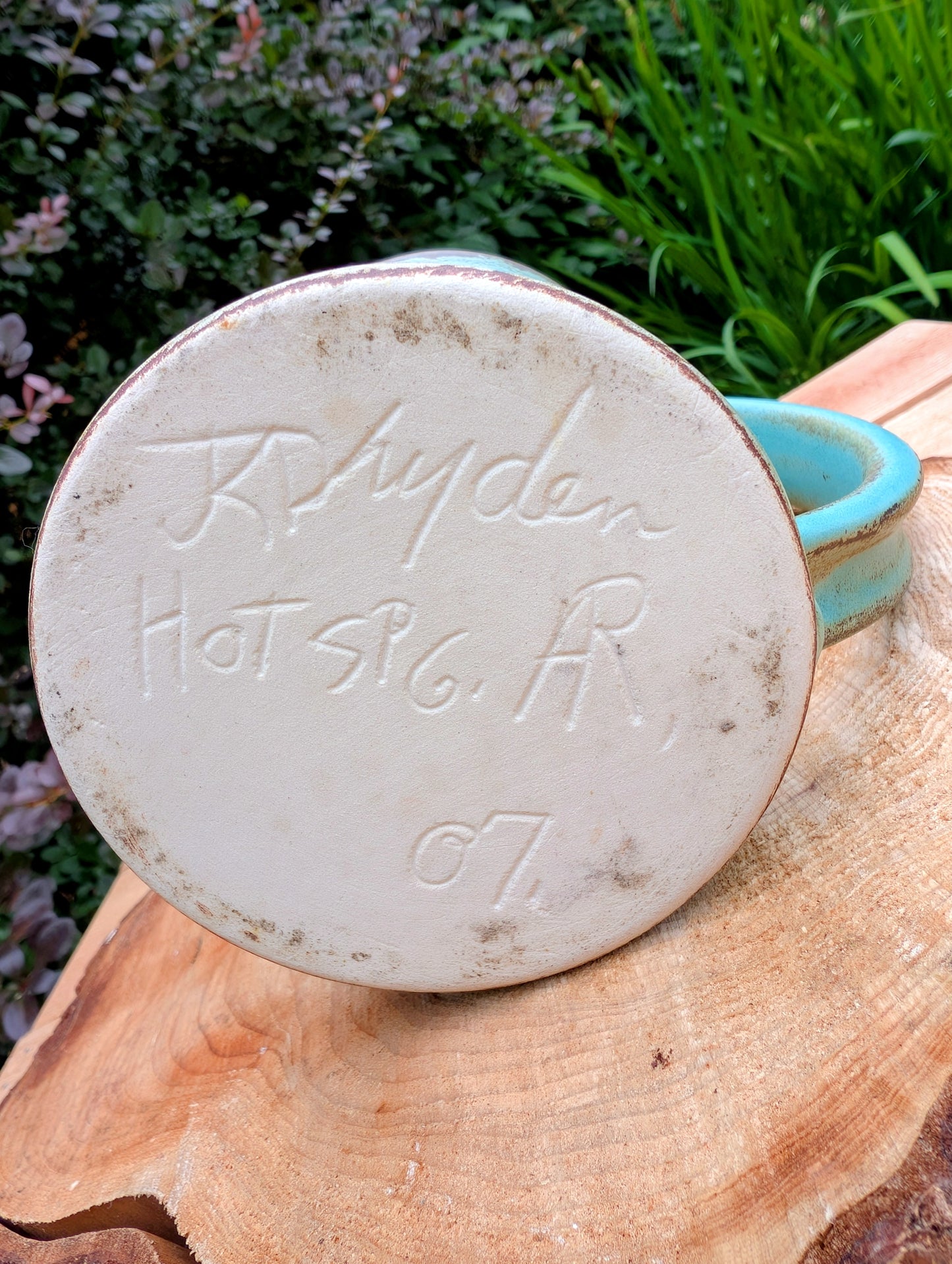 A beautifully handcrafted studio pottery tankard-style mug, wheel-thrown in Hot Springs, Arkansas and dated 2007. Its flowing turquoise, olive, and bronze glaze, generous size, and comfortable thumb-rest handle make it both a functional everyday piece and a collectible example of American studio pottery.