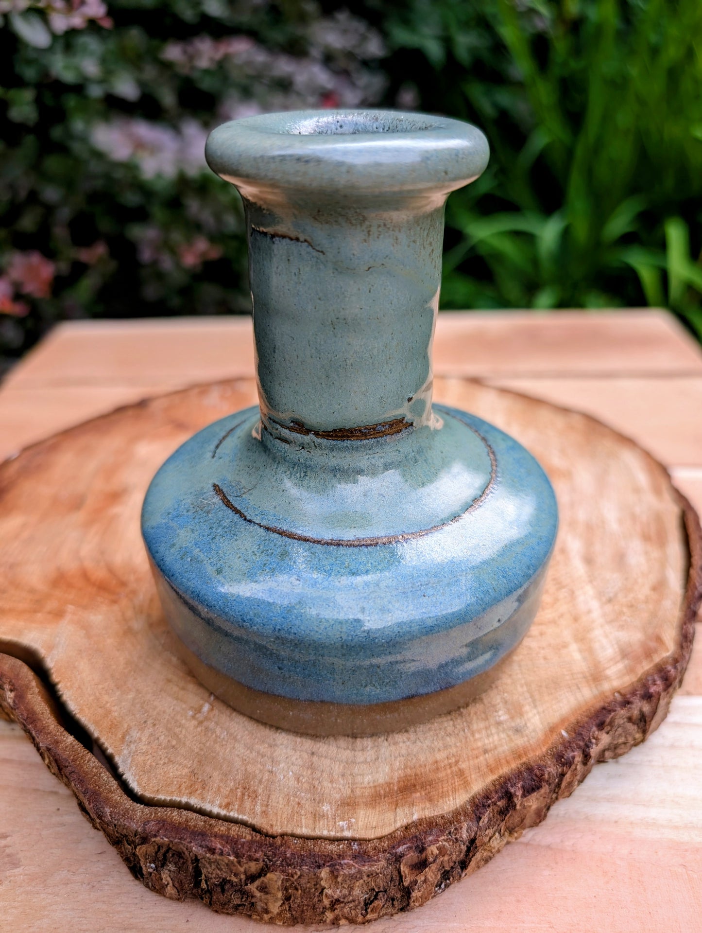 A beautifully hand-thrown studio pottery bud vase featuring a rich blue-green glaze over warm stoneware clay. Its timeless organic form makes it perfect for displaying a single bloom, dried botanicals, or as a sculptural accent in any room.