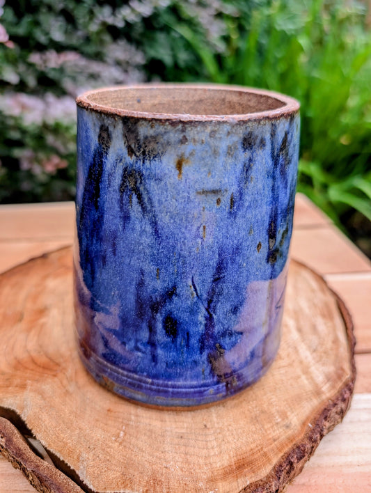 Hand-thrown and artist signed, this versatile stoneware vessel features a rich variegated cobalt blue glaze with an exposed stoneware rim that highlights its handcrafted character. Beautiful as a vase, utensil crock, brush holder, or decorative accent, it brings timeless studio craftsmanship to any home.