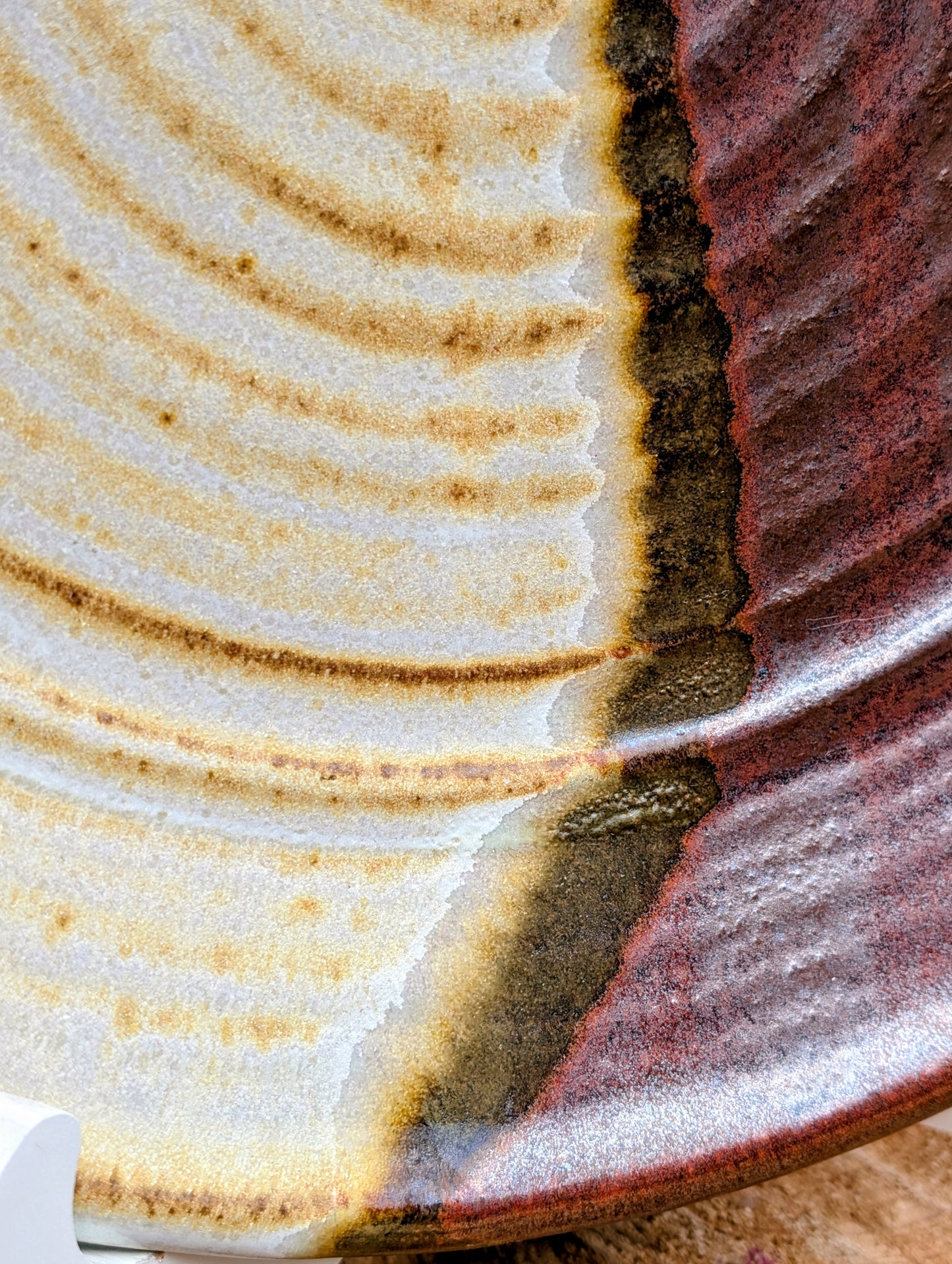 A striking hand-thrown studio pottery platter featuring an expressive cream, maroon, and olive glaze composition with visible throwing rings and an incised artist signature. Beautiful as both a decorative wall display and a functional serving piece, it embodies the warmth and craftsmanship of contemporary American studio ceramics.