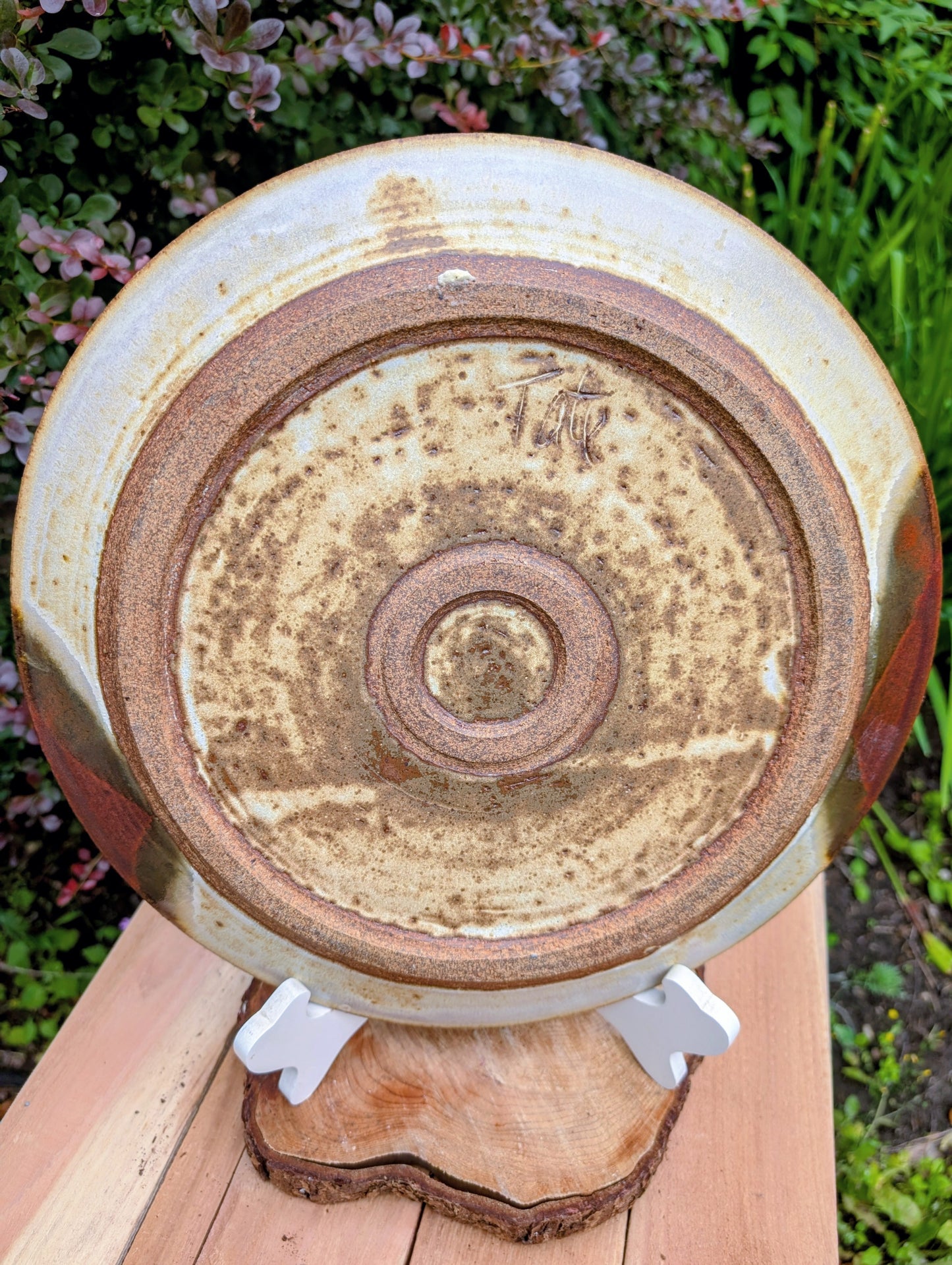 A striking hand-thrown studio pottery platter featuring an expressive cream, maroon, and olive glaze composition with visible throwing rings and an incised artist signature. Beautiful as both a decorative wall display and a functional serving piece, it embodies the warmth and craftsmanship of contemporary American studio ceramics.