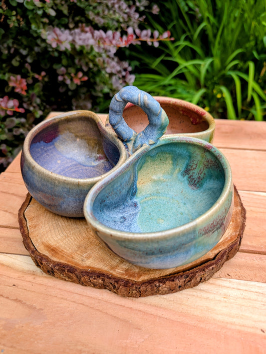 Beautifully handcrafted and artist signed, this three-bowl stoneware condiment server combines sculptural artistry with everyday functionality. Finished in layered seafoam, aqua, moss, and earthy glazes, it brings timeless craftsmanship and Pacific Northwest-inspired beauty to entertaining.