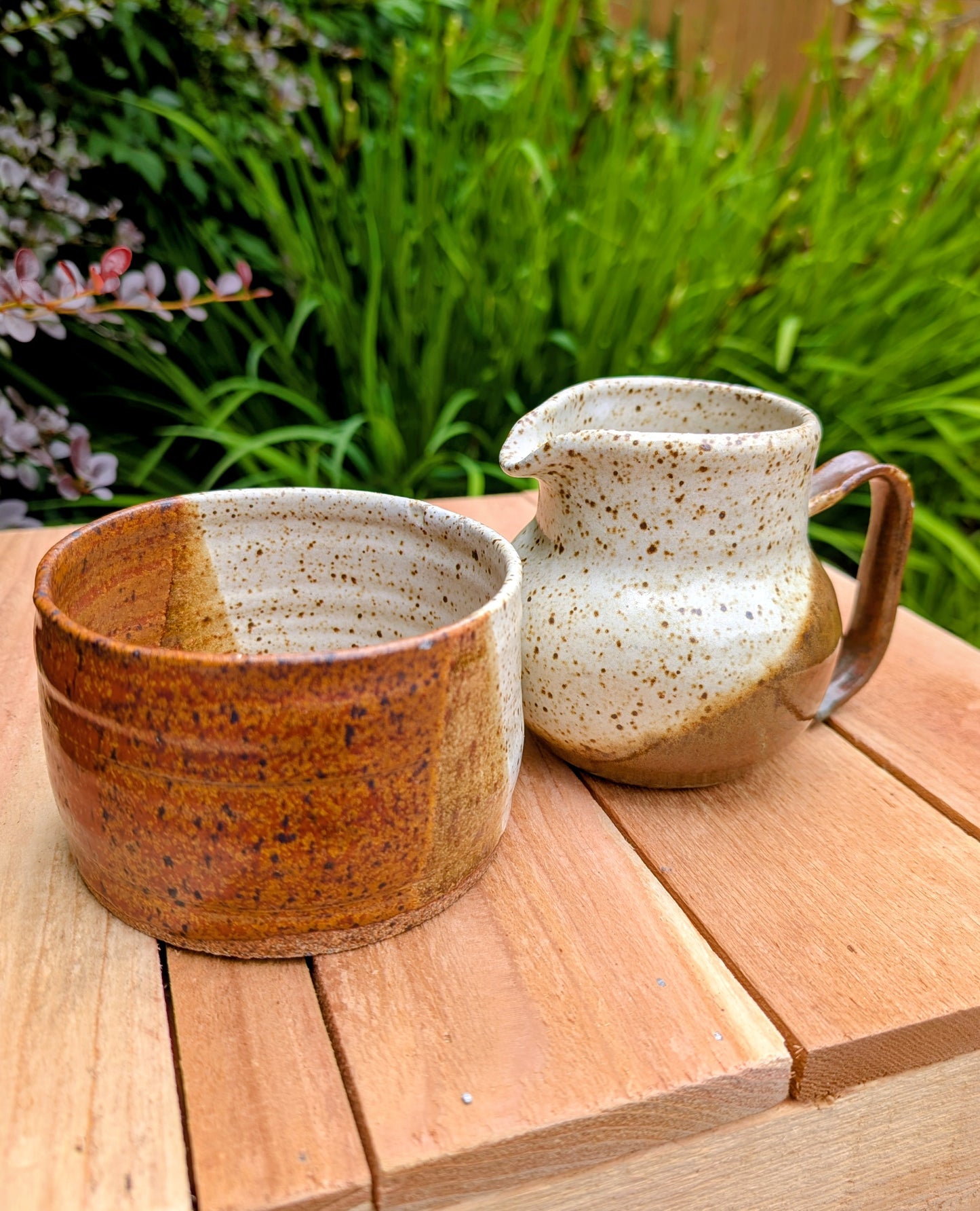 Bring handcrafted warmth to your table with this signed studio pottery creamer and sugar bowl set. Finished in a beautiful speckled cream glaze with flowing olive-brown accents, this artisan stoneware pair blends rustic craftsmanship with timeless everyday function.