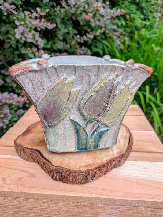 Celebrate handcrafted artistry with this handbuilt stoneware vase or cachepot featuring sculpted tulip relief panels, rich matte glazes, and an architectural four-footed form. Its organic botanical design makes it equally beautiful as a floral vessel, planter, or sculptural accent.