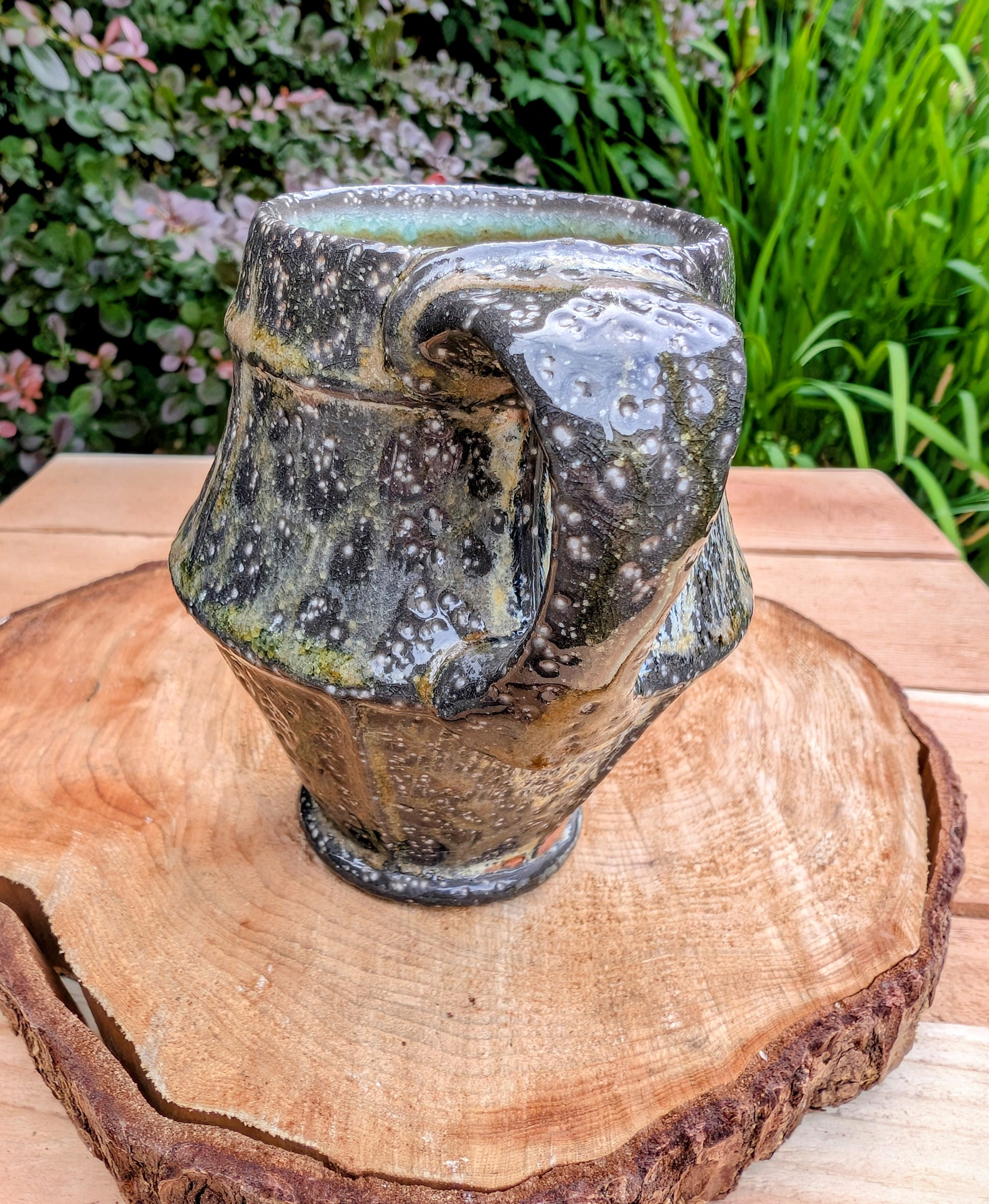 Celebrate slow mornings with this handcrafted faceted studio pottery mug, featuring a richly layered volcanic glaze and a soft celadon-green interior. Its sculptural form and earthy palette make it equally beautiful in the hand or displayed as functional art.