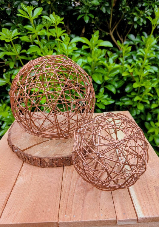 Bring warmth and texture to your home with this coordinated set of two copper-tone woven metal decorative spheres. Their sculptural open-weave design complements modern organic, farmhouse, industrial, and contemporary interiors, making them versatile accents for shelves, coffee tables, decorative bowls, and centerpieces.