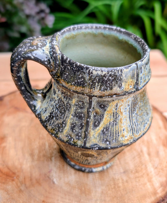 Celebrate slow mornings with this handcrafted faceted studio pottery mug, featuring a richly layered volcanic glaze and a soft celadon-green interior. Its sculptural form and earthy palette make it equally beautiful in the hand or displayed as functional art.