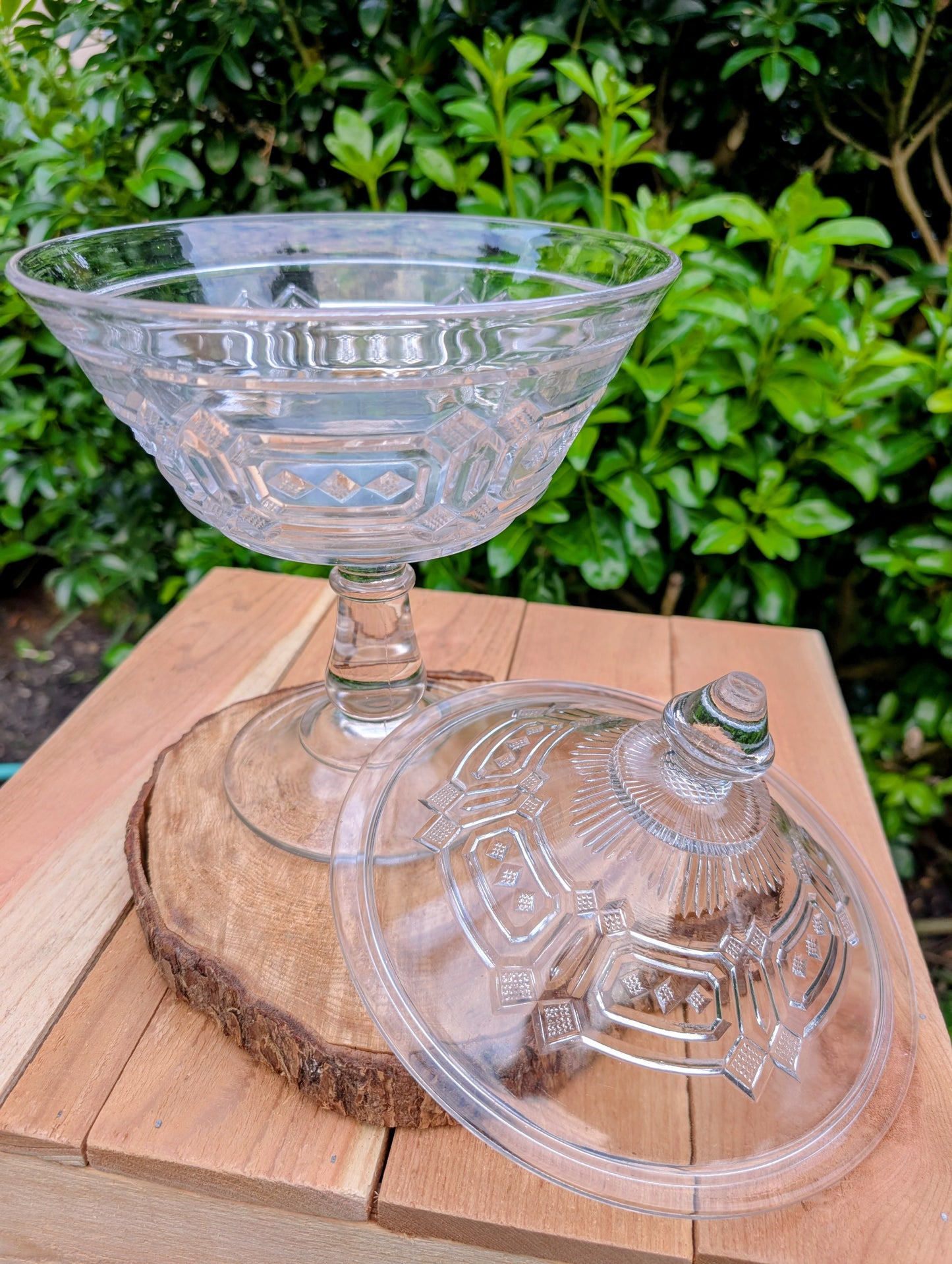 An elegant early 20th-century pressed glass covered compote featuring bold geometric Art Deco styling and a striking pedestal silhouette. Although the pedestal has visible stress cracks, the original lid, impressive scale, and architectural design make it a beautiful decorative display piece.