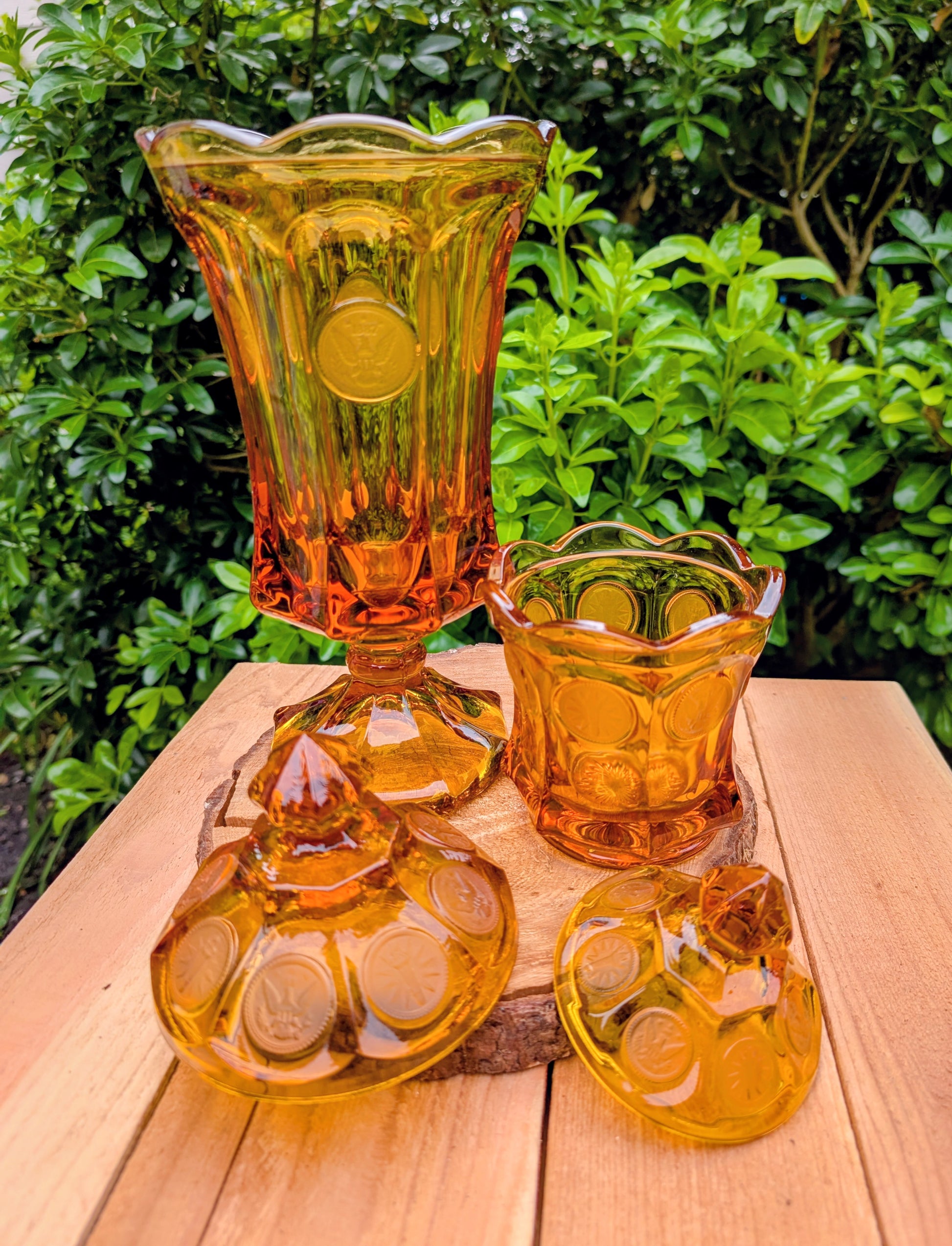 A stunning matching set of vintage Indiana Glass in the iconic Kings Crown (Coin) pattern. This coordinated amber glass collection includes a covered pedestal vase and matching covered candy dish, each with its original lid. A beautiful Mid-Century display for collectors and vintage home décor enthusiasts.