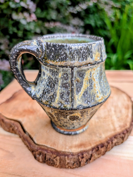 Celebrate slow mornings with this handcrafted faceted studio pottery mug, featuring a richly layered volcanic glaze and a soft celadon-green interior. Its sculptural form and earthy palette make it equally beautiful in the hand or displayed as functional art.