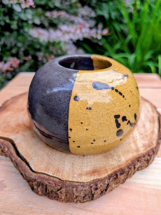 A beautifully hand-thrown studio pottery bud vase dated 1988, featuring a striking half-black, half-mustard glaze accented with expressive iron oxide speckling. Its sculptural form and organic craftsmanship make it equally at home as a minimalist floral vessel or standalone work of ceramic art.