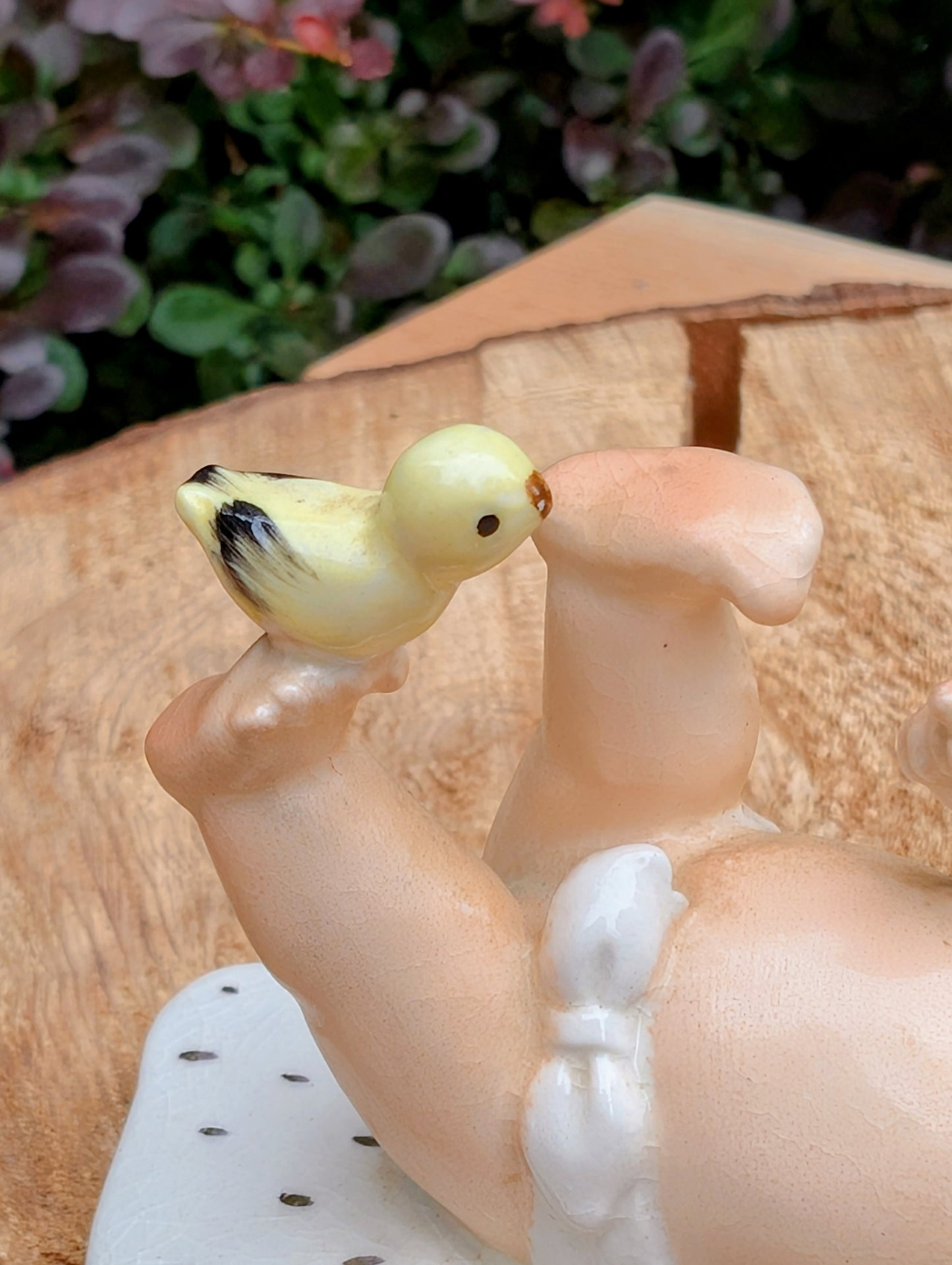 A close-up of a decorative figurine showing a pale peach-toned baby body with white diaper area and a small pale yellow bird with black wing details perched on the foot.