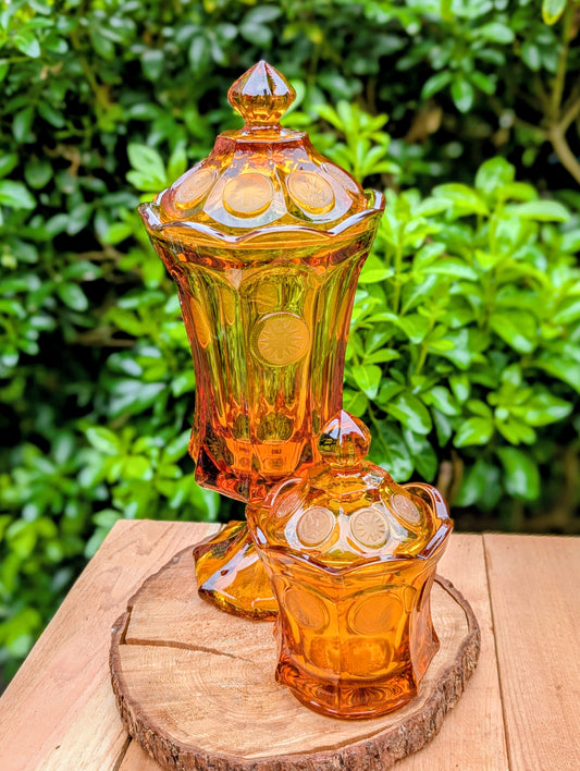 A stunning matching set of vintage Indiana Glass in the iconic Kings Crown (Coin) pattern. This coordinated amber glass collection includes a covered pedestal vase and matching covered candy dish, each with its original lid. A beautiful Mid-Century display for collectors and vintage home décor enthusiasts.