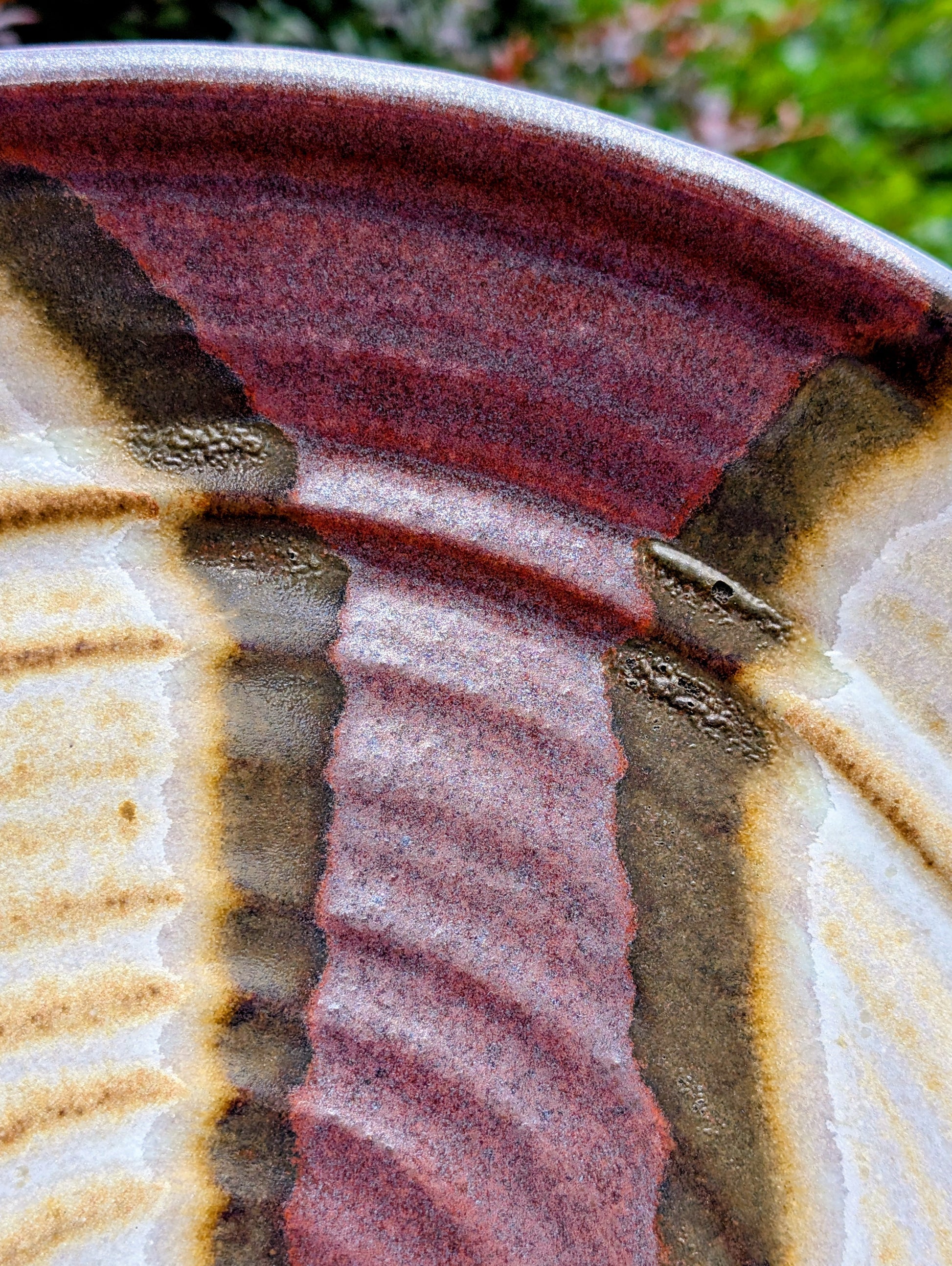 A striking hand-thrown studio pottery platter featuring an expressive cream, maroon, and olive glaze composition with visible throwing rings and an incised artist signature. Beautiful as both a decorative wall display and a functional serving piece, it embodies the warmth and craftsmanship of contemporary American studio ceramics.