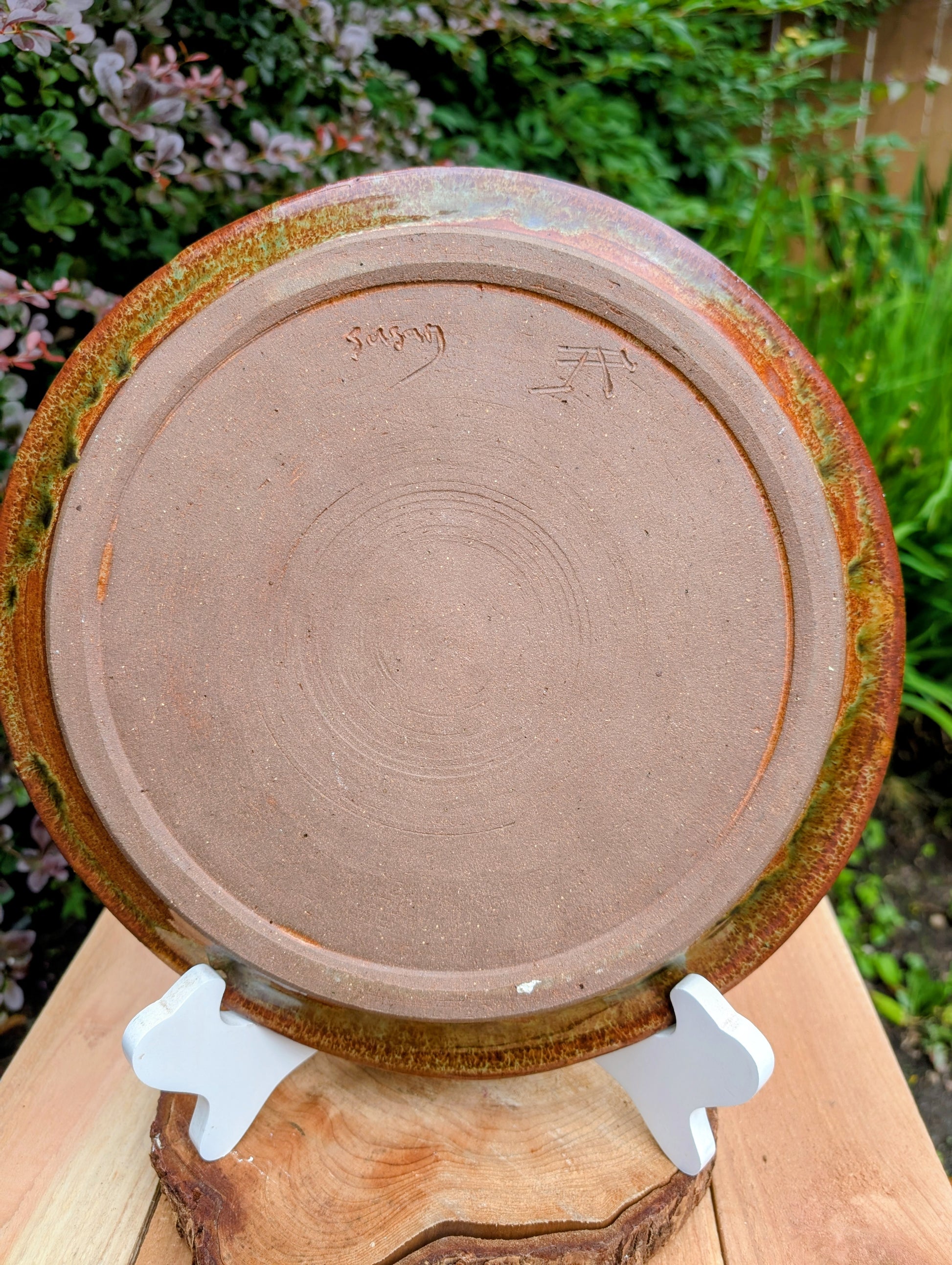 A beautifully hand-thrown studio pottery charger featuring an impressed spiral design and richly variegated moss green and rust glazes. This substantial signed stoneware piece brings timeless craftsmanship and Pacific Northwest-inspired warmth to shelves, tables, or wall displays.
