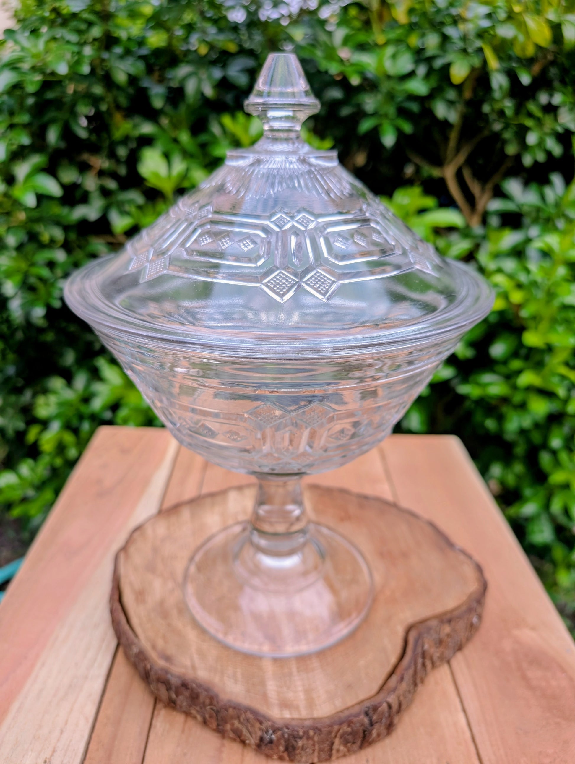 An elegant early 20th-century pressed glass covered compote featuring bold geometric Art Deco styling and a striking pedestal silhouette. Although the pedestal has visible stress cracks, the original lid, impressive scale, and architectural design make it a beautiful decorative display piece.