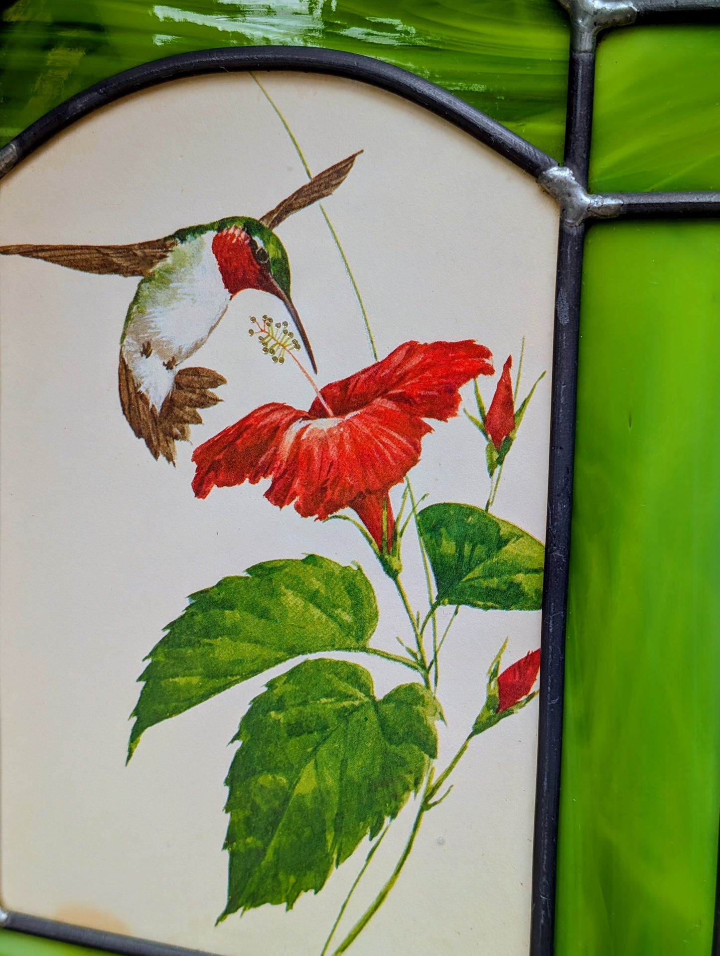 Bring the beauty of a hummingbird in bloom into your home with this handcrafted stained glass hanging panel. Featuring vibrant textured art glass surrounding a detailed hummingbird and hibiscus centerpiece, it catches natural light beautifully and adds year-round color to any window, sunroom, or garden-inspired space.