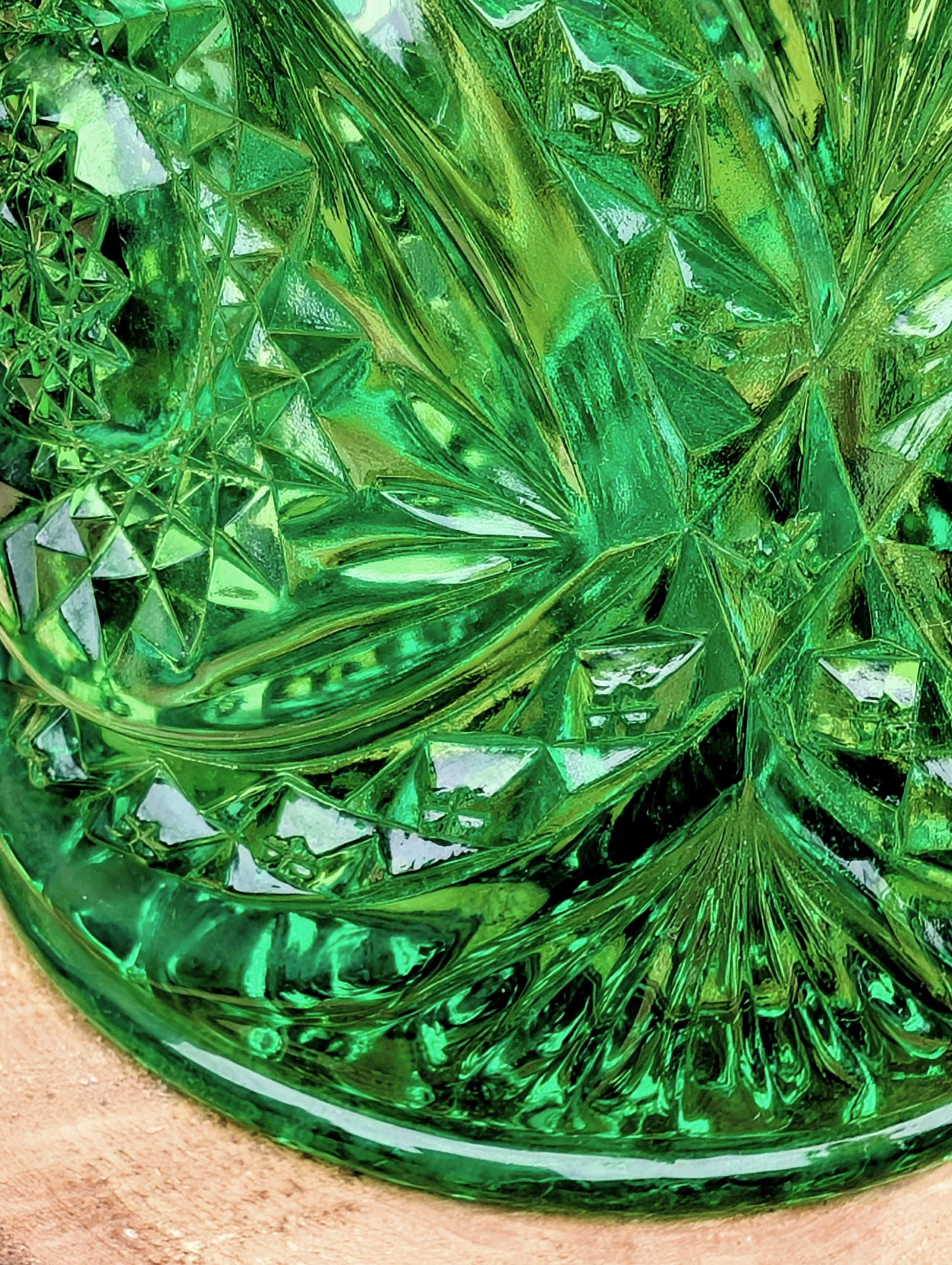 A close-up of a green cut-glass dish or bowl with a faceted starburst pattern, resting on a light wood surface.