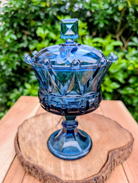 A striking vintage Fostoria Windsor Crown covered chalice in vibrant Royal Blue glass, produced during the early 1960s. With its sculptural pedestal, jewel-like crown rim, and original domed lid, this elegant candy dish is equally at home as a display centerpiece or functional serving piece.