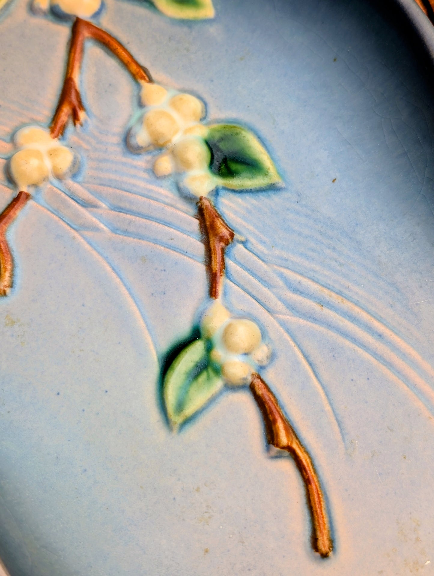Close-up of a light blue ceramic surface with embossed floral details, including white blossoms, green leaves, and brown stems.