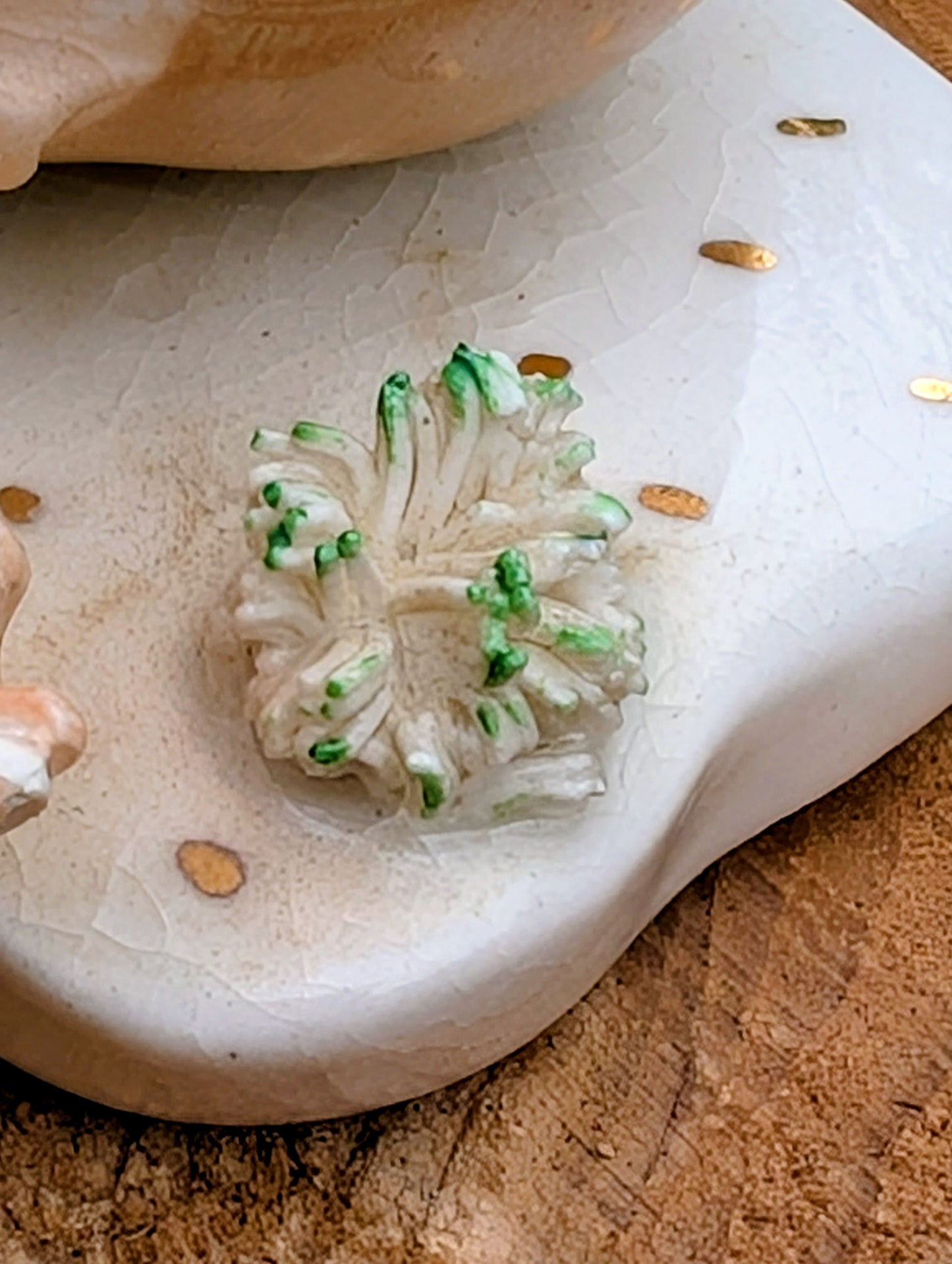 A small sculptural floral ornament or decorative piece in translucent white with bright green accents, displayed on a textured off-white stone slab over a brown wooden surface.