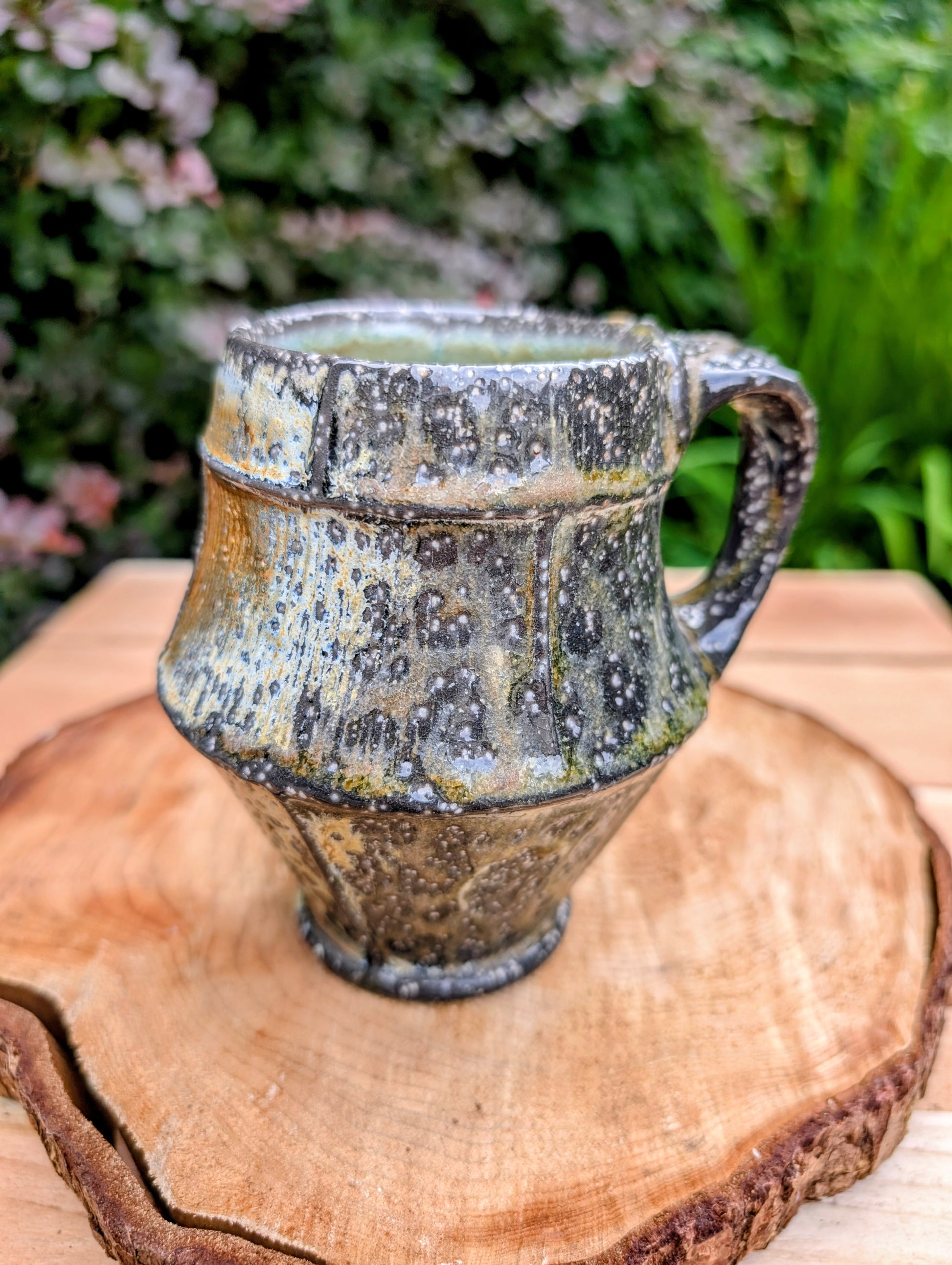 Celebrate slow mornings with this handcrafted faceted studio pottery mug, featuring a richly layered volcanic glaze and a soft celadon-green interior. Its sculptural form and earthy palette make it equally beautiful in the hand or displayed as functional art.