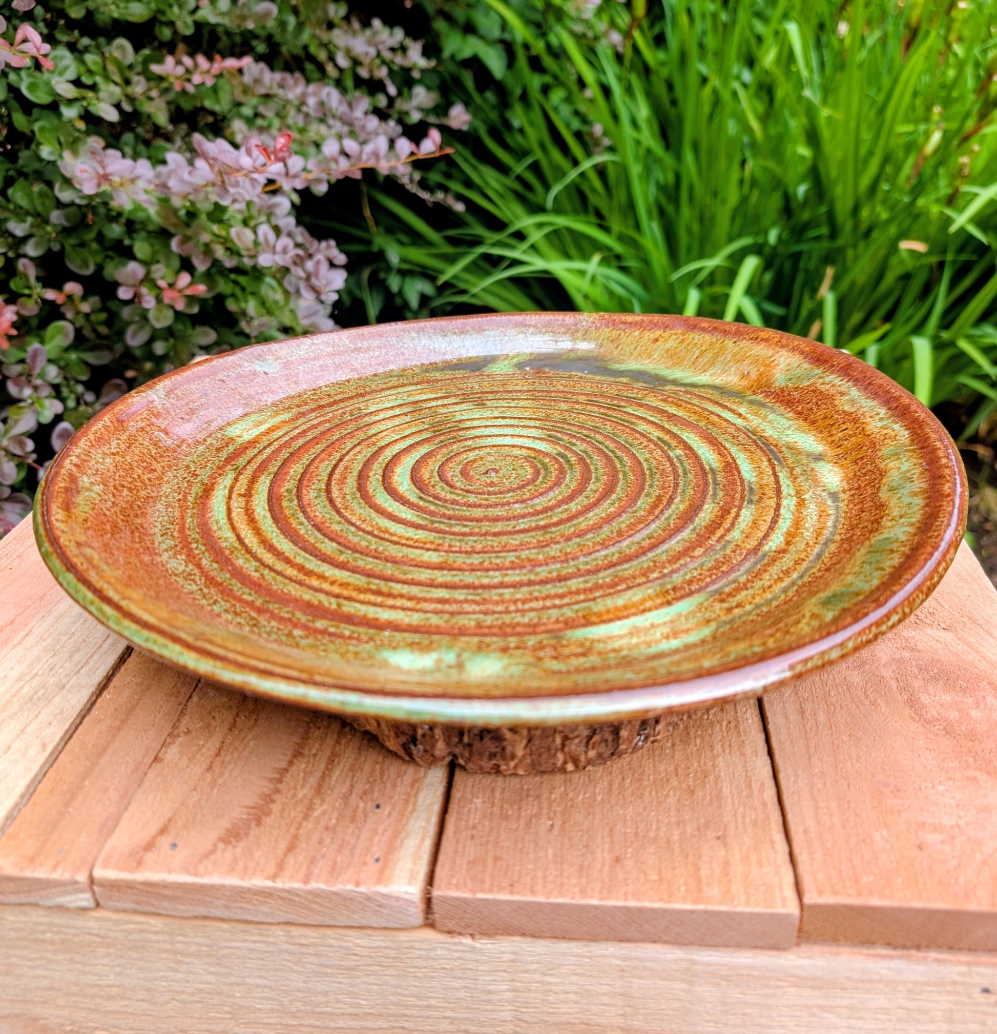 A beautifully hand-thrown studio pottery charger featuring an impressed spiral design and richly variegated moss green and rust glazes. This substantial signed stoneware piece brings timeless craftsmanship and Pacific Northwest-inspired warmth to shelves, tables, or wall displays.