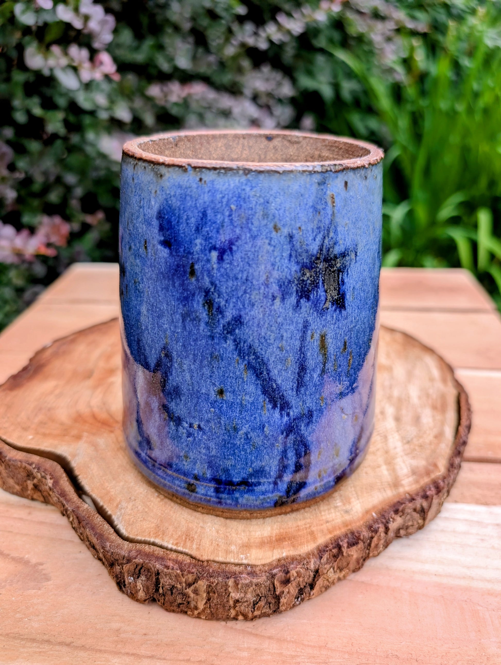 Hand-thrown and artist signed, this versatile stoneware vessel features a rich variegated cobalt blue glaze with an exposed stoneware rim that highlights its handcrafted character. Beautiful as a vase, utensil crock, brush holder, or decorative accent, it brings timeless studio craftsmanship to any home.
